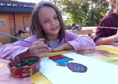 Mila malt mit Acrylfarben einen Heißluftballon. In dem Korb des Heißluftballons sitzt ein Mädchen.